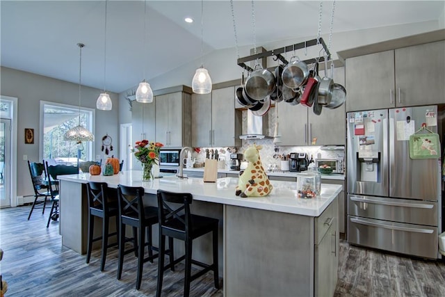 kitchen with lofted ceiling, a center island with sink, appliances with stainless steel finishes, and hanging light fixtures