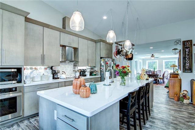 kitchen featuring a kitchen island with sink, stainless steel appliances, lofted ceiling, and wall chimney range hood