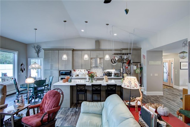 kitchen with dark wood-type flooring, vaulted ceiling, wall chimney exhaust hood, appliances with stainless steel finishes, and decorative light fixtures