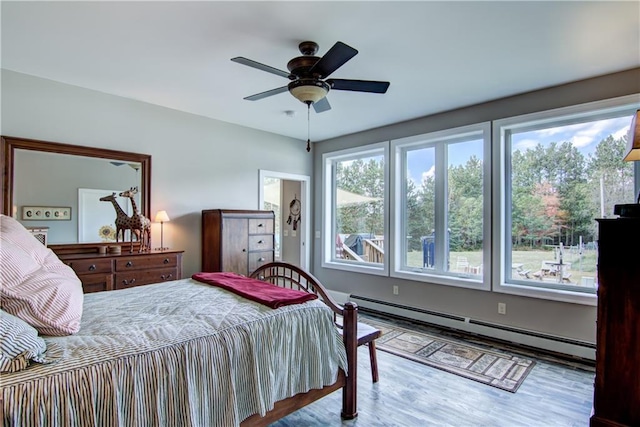 bedroom with hardwood / wood-style floors, a baseboard heating unit, and ceiling fan