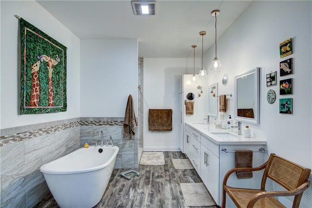 bathroom with tile walls, vanity, wood-type flooring, and a bathing tub