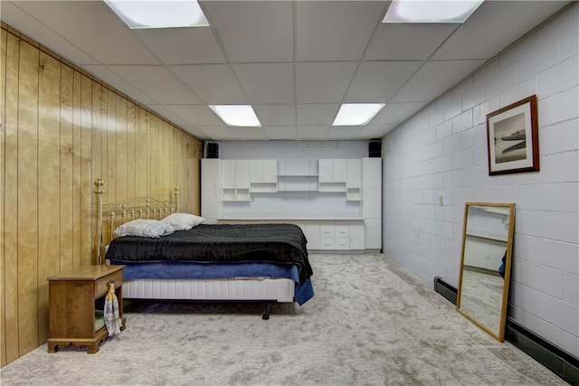 bedroom with a drop ceiling, wood walls, and light colored carpet