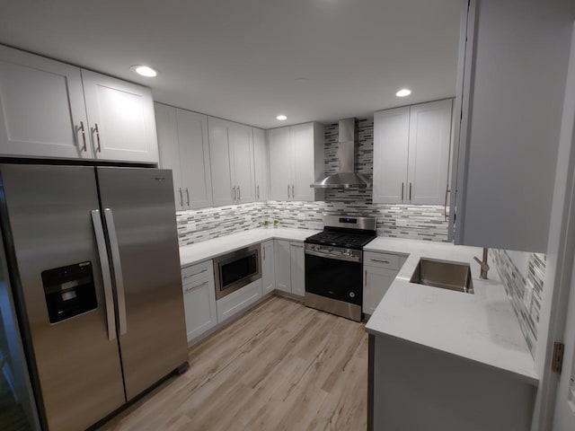 kitchen with decorative backsplash, wall chimney range hood, white cabinetry, appliances with stainless steel finishes, and light hardwood / wood-style floors