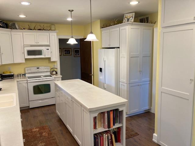 kitchen with white cabinets, hanging light fixtures, dark hardwood / wood-style floors, and white appliances