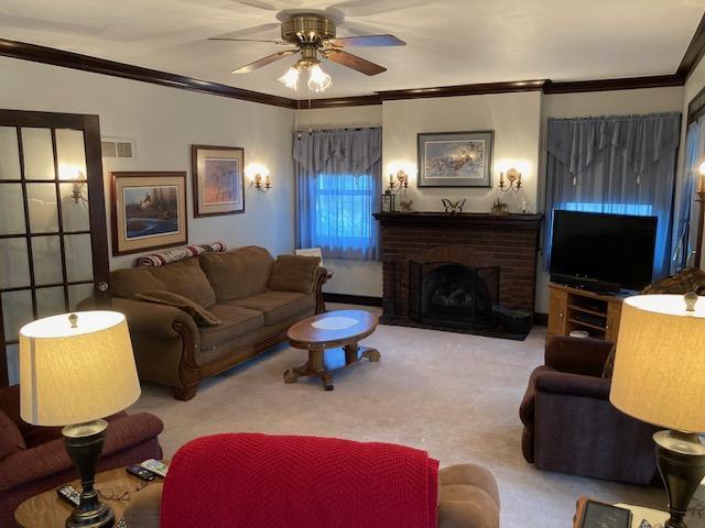 living room with ceiling fan, a fireplace, light carpet, and crown molding