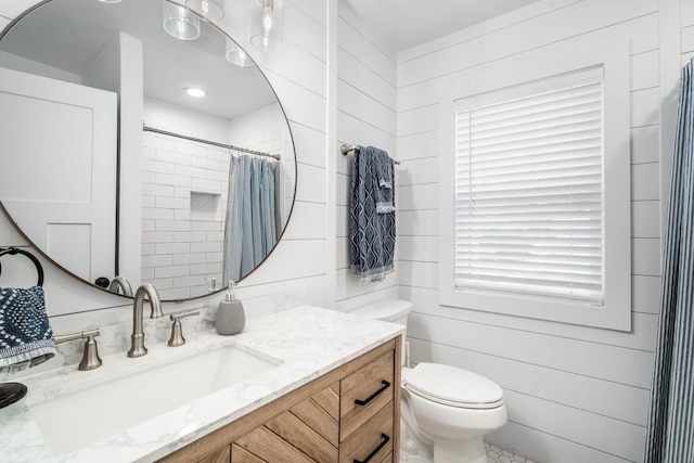 bathroom with a healthy amount of sunlight, wooden walls, vanity, and toilet