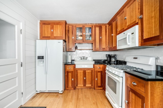 kitchen with light wood-type flooring, sink, decorative backsplash, wooden walls, and white appliances