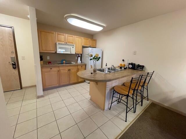 kitchen with light tile patterned flooring, kitchen peninsula, a kitchen breakfast bar, white appliances, and light brown cabinets