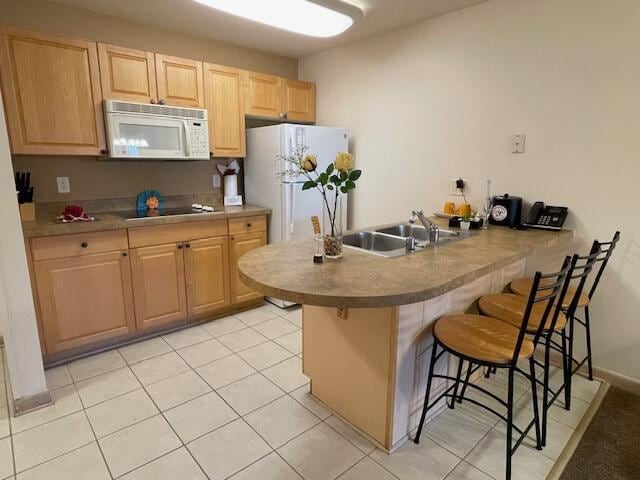 kitchen featuring light tile patterned flooring, kitchen peninsula, white appliances, light brown cabinetry, and a breakfast bar area