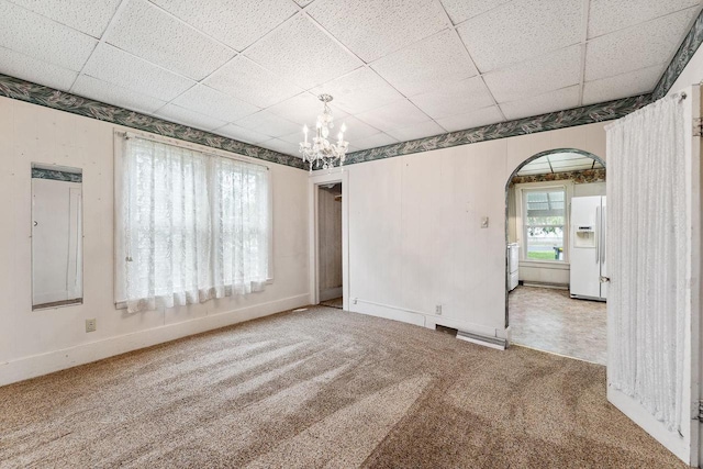 carpeted empty room with an inviting chandelier and a paneled ceiling