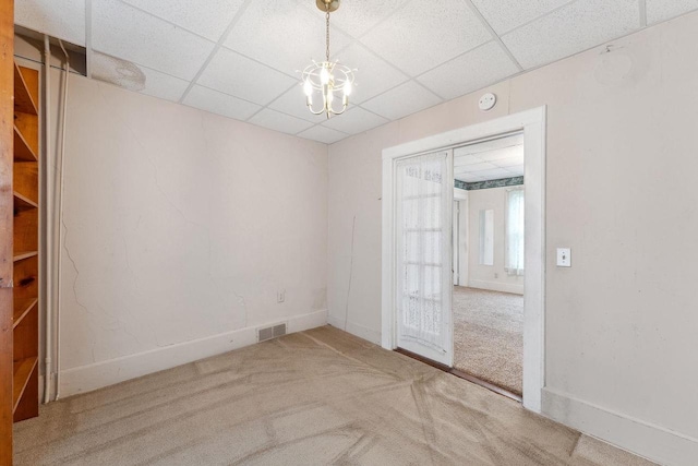 carpeted spare room with a drop ceiling and an inviting chandelier