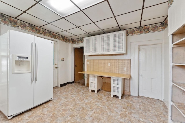 kitchen with a drop ceiling, white fridge with ice dispenser, and white cabinetry