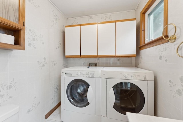 clothes washing area with tile walls, separate washer and dryer, and cabinets