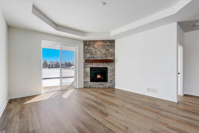 unfurnished living room featuring a raised ceiling, a fireplace, and light hardwood / wood-style floors