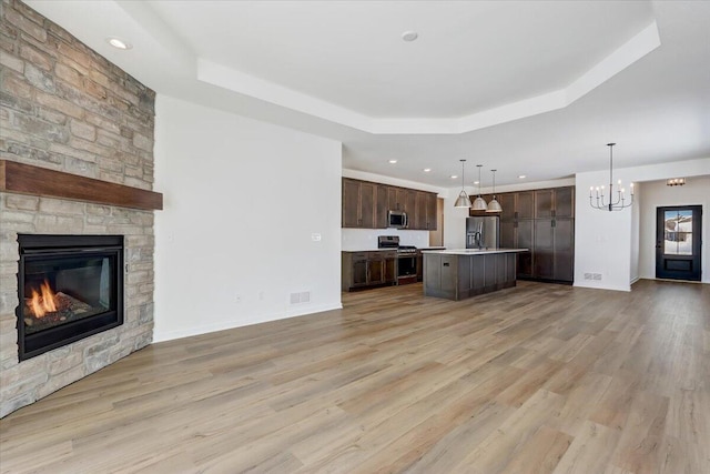 kitchen with a fireplace, a kitchen island, a raised ceiling, and stainless steel appliances