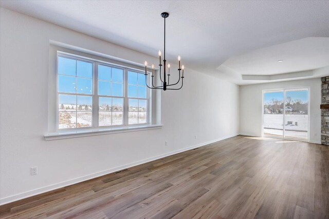 unfurnished dining area featuring a chandelier, hardwood / wood-style flooring, and a tray ceiling