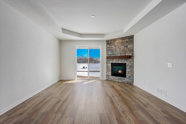 unfurnished living room with a raised ceiling, a textured ceiling, hardwood / wood-style flooring, and a stone fireplace