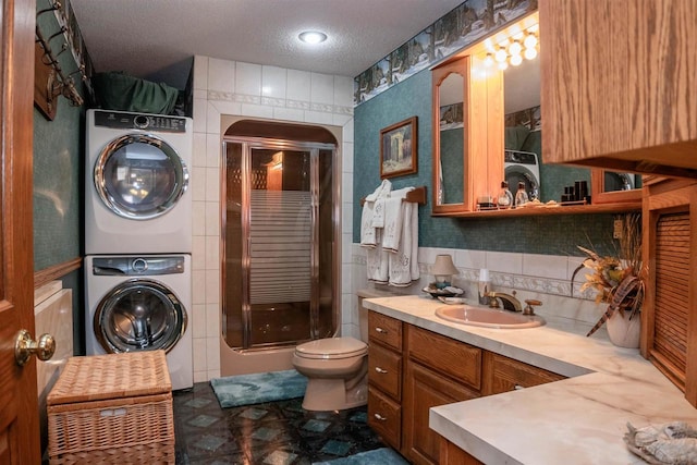 bathroom featuring vanity, a textured ceiling, stacked washer and dryer, toilet, and a shower with shower door