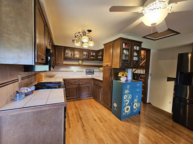 kitchen with tile countertops, dark brown cabinets, ceiling fan, light hardwood / wood-style flooring, and fridge with ice dispenser