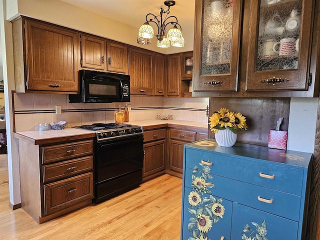 kitchen featuring pendant lighting, light hardwood / wood-style flooring, decorative backsplash, black appliances, and an inviting chandelier