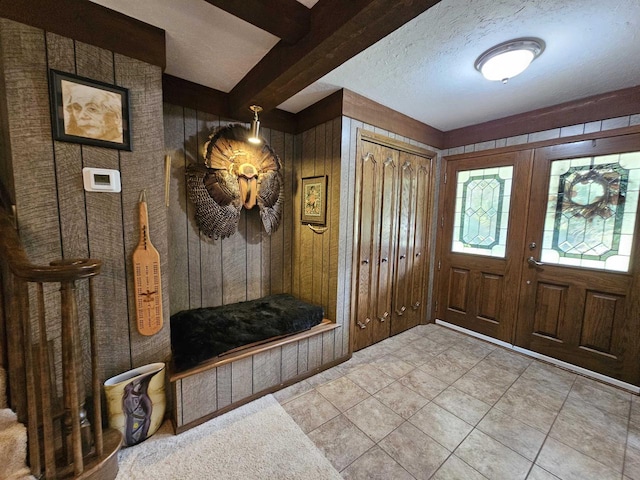 entrance foyer featuring a textured ceiling, beamed ceiling, wood walls, light tile patterned floors, and french doors