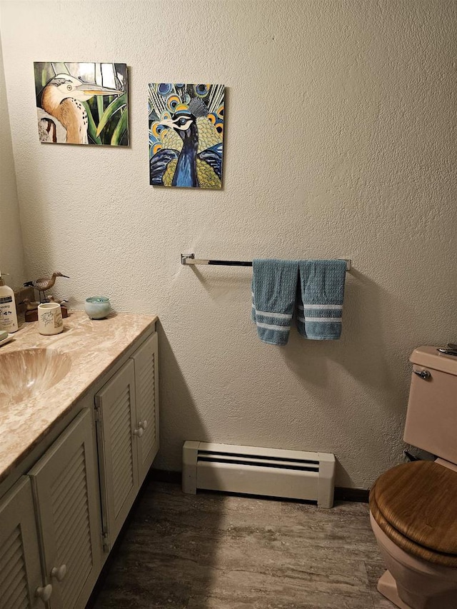 bathroom featuring wood-type flooring, toilet, vanity, and baseboard heating