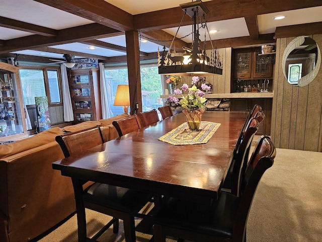 dining area with carpet floors, sink, ceiling fan with notable chandelier, and beam ceiling