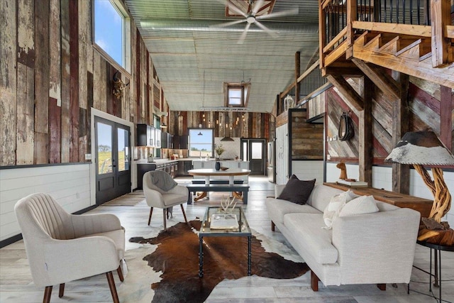 living room featuring french doors, wooden walls, light hardwood / wood-style floors, and a high ceiling