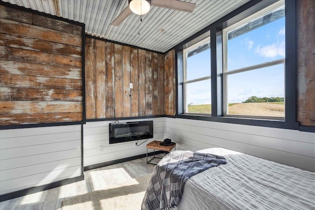 bedroom with ceiling fan, light hardwood / wood-style floors, and wood walls