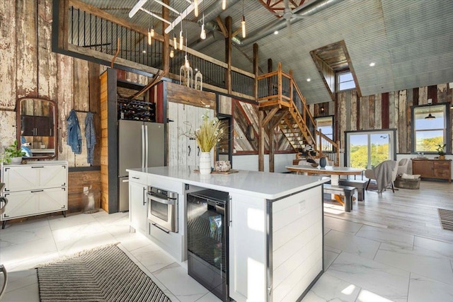 kitchen with white cabinetry, high vaulted ceiling, appliances with stainless steel finishes, wooden walls, and beverage cooler