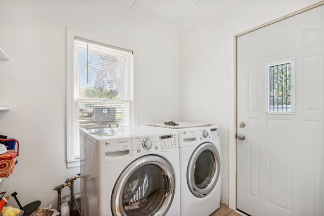 clothes washing area featuring light tile patterned flooring, washing machine and dryer, and a healthy amount of sunlight