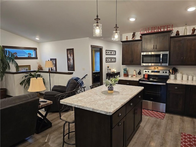 kitchen featuring wood-type flooring, hanging light fixtures, a kitchen island, stainless steel appliances, and dark brown cabinetry