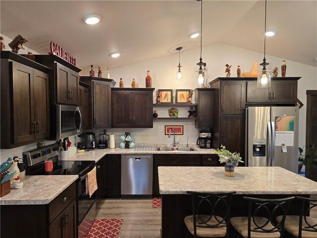 kitchen featuring sink, vaulted ceiling, hanging light fixtures, a kitchen island, and appliances with stainless steel finishes