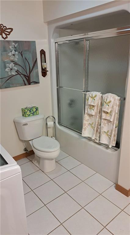 bathroom with tile patterned flooring, bath / shower combo with glass door, and toilet