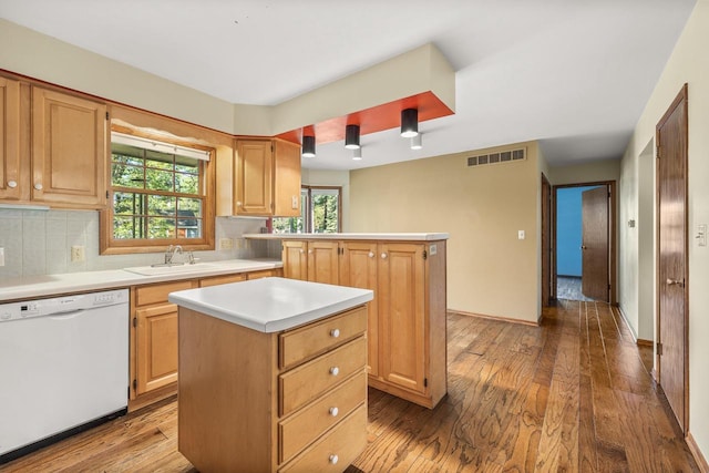 kitchen with sink, tasteful backsplash, light hardwood / wood-style flooring, dishwasher, and a center island