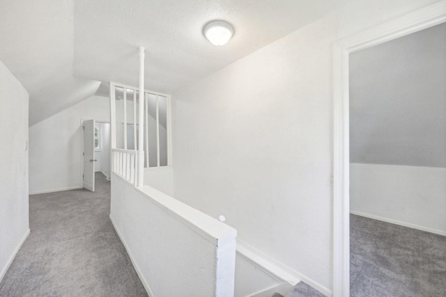 hall featuring a textured ceiling, lofted ceiling, and light carpet