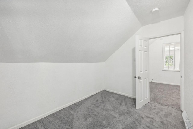 bonus room with a textured ceiling, vaulted ceiling, and light carpet