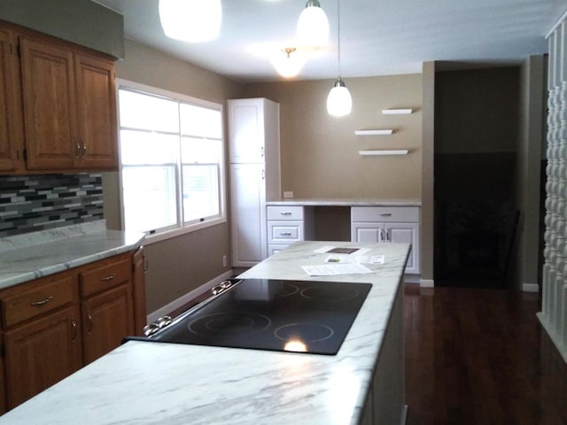 kitchen with pendant lighting, light stone counters, built in desk, black electric cooktop, and decorative backsplash