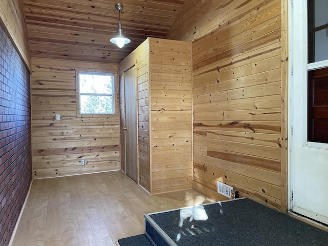 empty room with light wood-type flooring, wood ceiling, wooden walls, and lofted ceiling