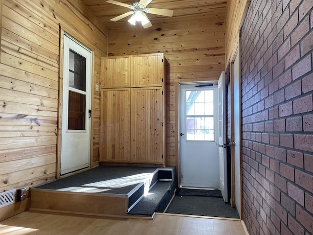 interior space with ceiling fan, wood walls, and brick wall