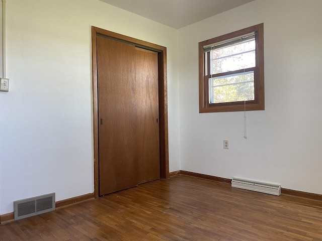 unfurnished bedroom with a baseboard heating unit, a closet, and dark hardwood / wood-style flooring