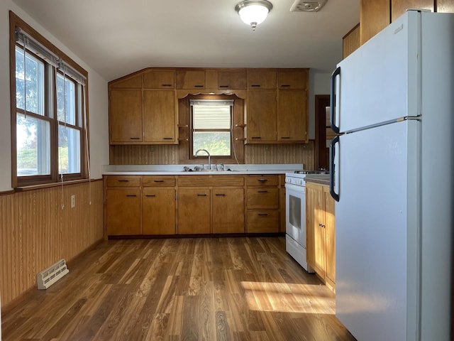 kitchen with white appliances, wooden walls, sink, and hardwood / wood-style flooring