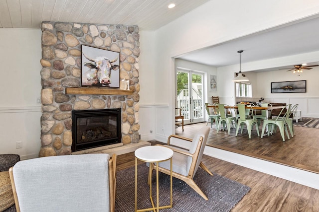 living room with wood-type flooring, a stone fireplace, wood ceiling, and ceiling fan