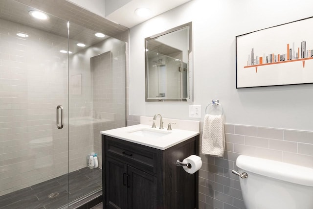 bathroom with tile walls, a shower with shower door, vanity, and toilet