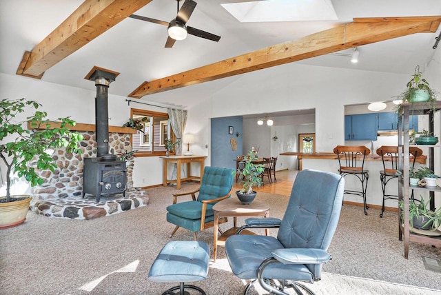 living room with ceiling fan, beamed ceiling, a wood stove, high vaulted ceiling, and light carpet