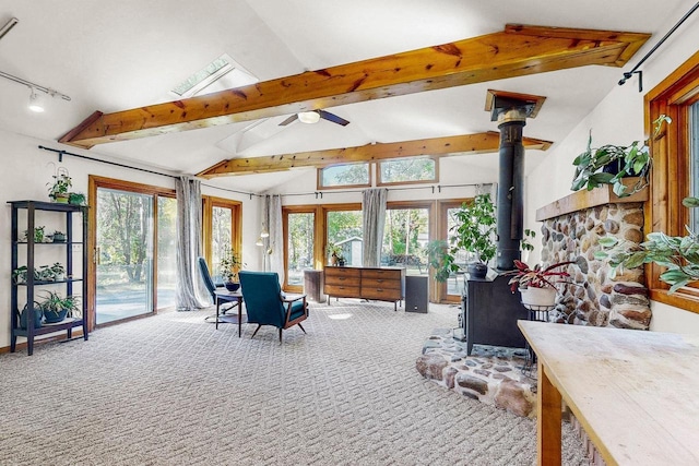 sunroom with plenty of natural light, ceiling fan, lofted ceiling with beams, and a wood stove