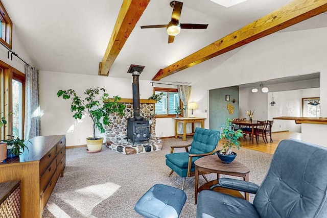 living room featuring light carpet, ceiling fan, vaulted ceiling with beams, and a wood stove