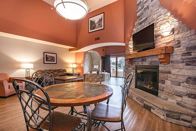 dining area featuring light wood-type flooring, a stone fireplace, and a high ceiling