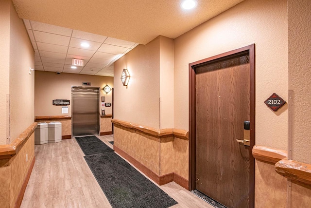 hallway featuring light wood-type flooring, elevator, and a paneled ceiling