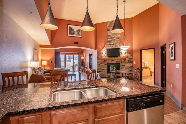 kitchen featuring sink, a stone fireplace, decorative light fixtures, dishwasher, and light wood-type flooring